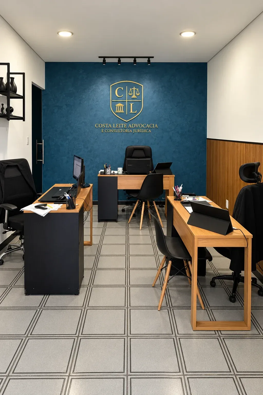 Sala do escritório: parede azul com o brasão dourado e o nome Costa Leite Advocacia, mesas de madeira e cadeiras pretas.